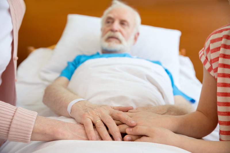 grandmother and grandfather holding hands with patient lying in hospital bed in clinic Person-Centered Home Care