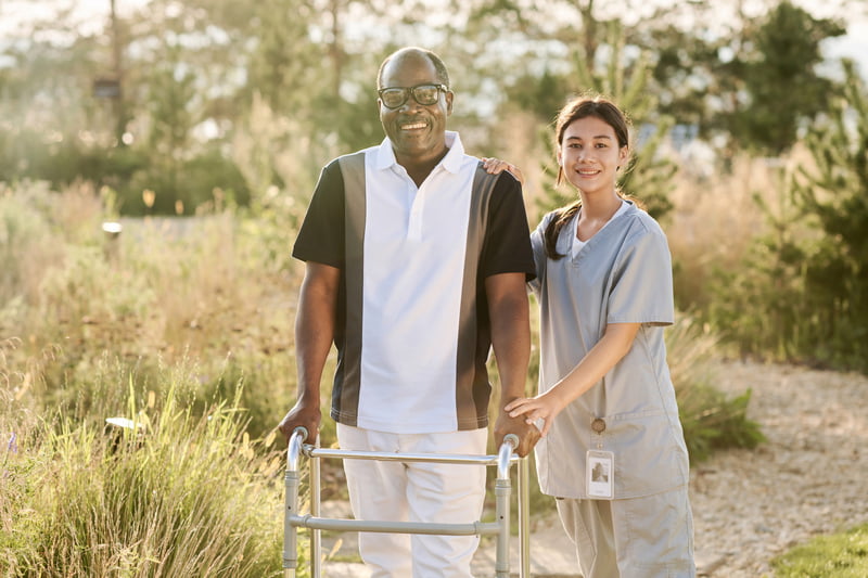 Senior man walking outdoors with nurse Disability Care